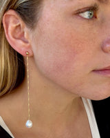 Close-up of a woman wearing a gold earring with a pearl drop.